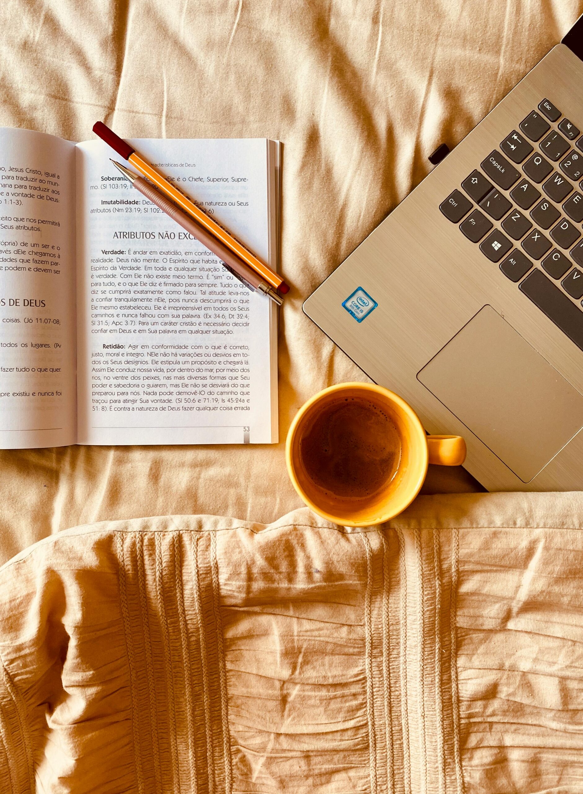 cup of coffee and computer on a bed next to a book